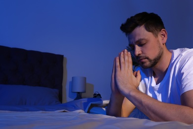 Photo of Handsome man saying bedtime prayer in dark room at night. Space for text