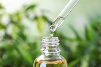 Photo of Dropping essential oil into glass bottle on blurred background, closeup