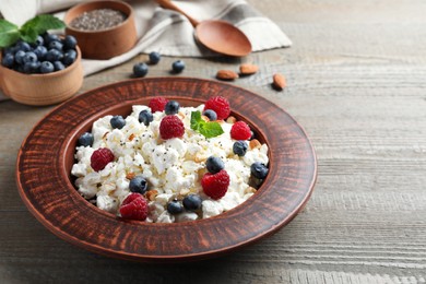 Photo of Fresh cottage cheese with berries and mint in plate on wooden table