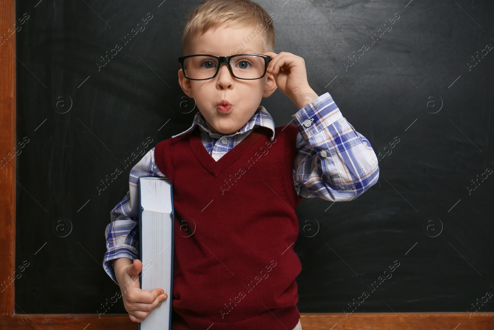 Photo of Cute little child wearing glasses near chalkboard. First time at school