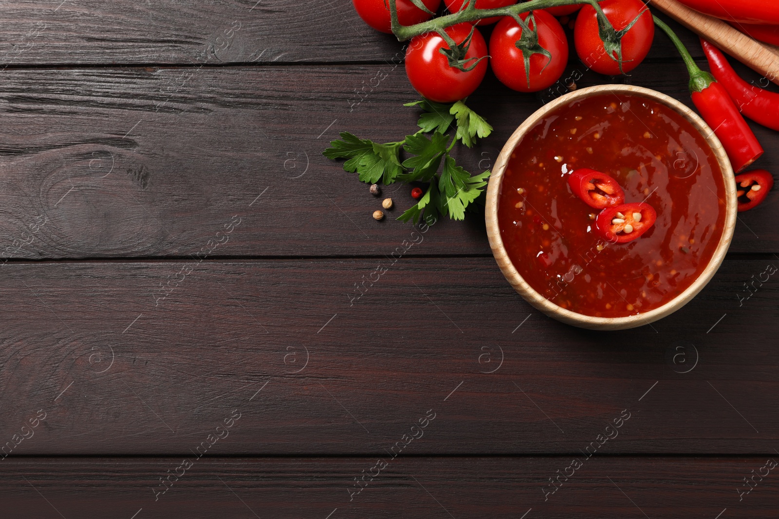 Photo of Spicy chili sauce and ingredients on wooden table, flat lay. Space for text