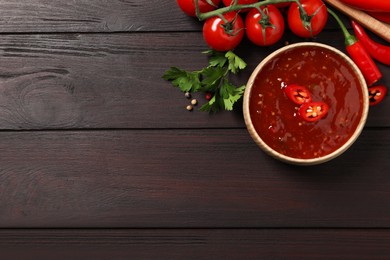 Photo of Spicy chili sauce and ingredients on wooden table, flat lay. Space for text