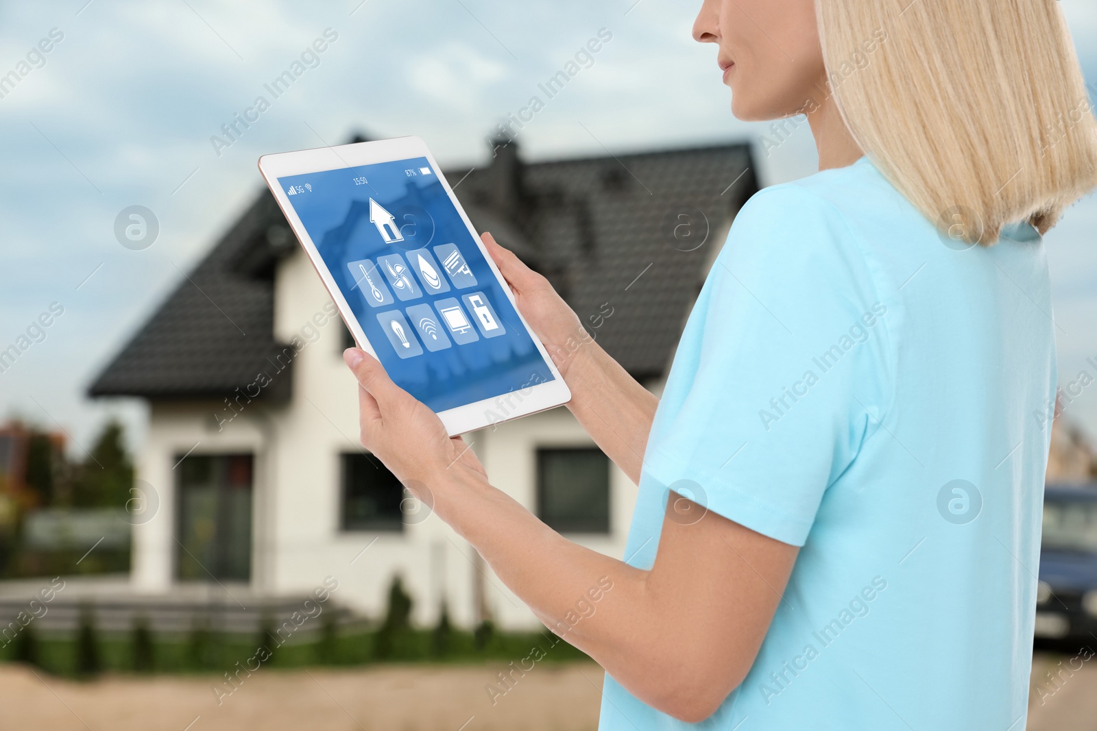Image of Woman using smart home control system via tablet near house outdoors, closeup