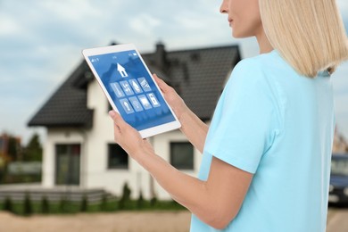 Woman using smart home control system via tablet near house outdoors, closeup