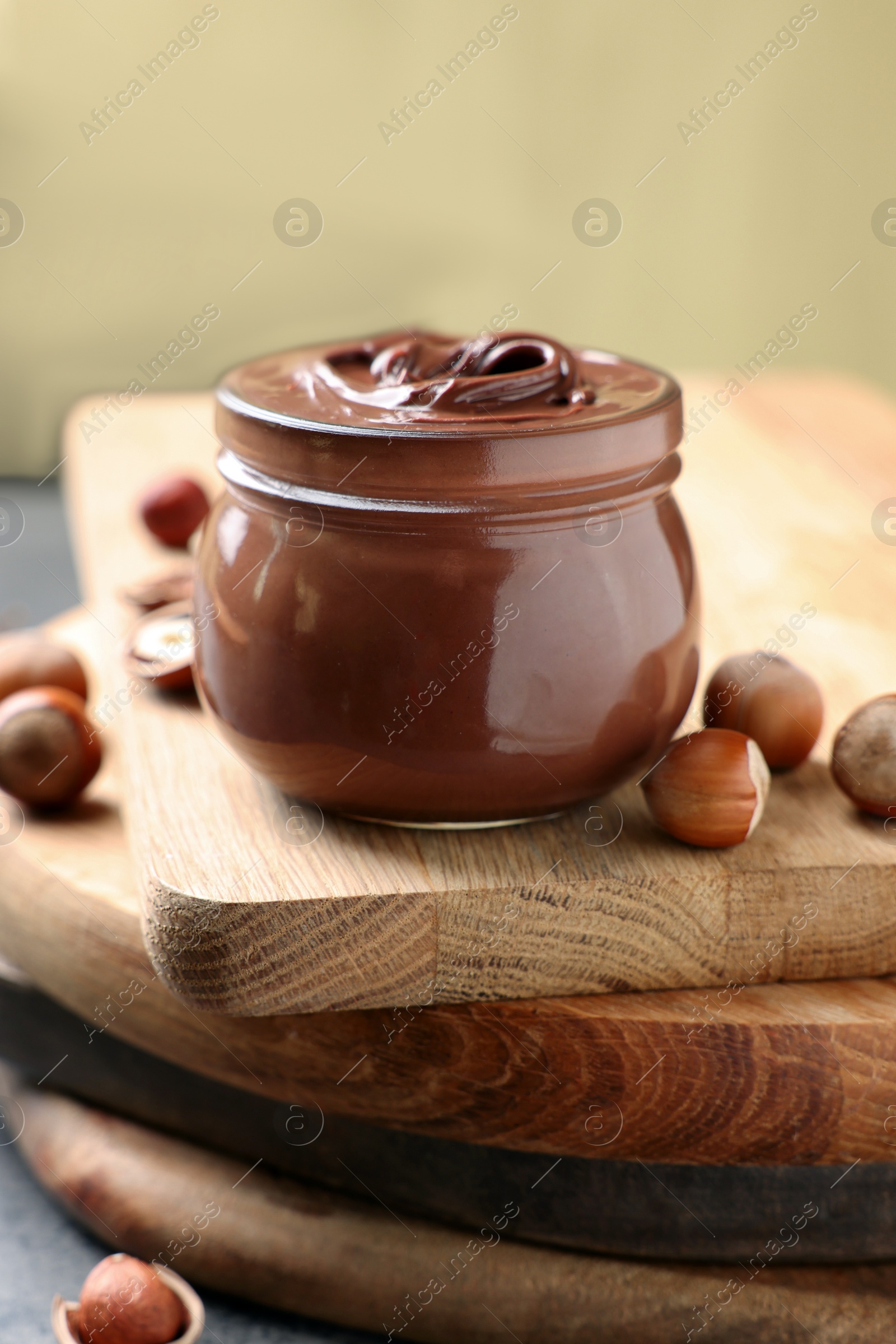 Photo of Glass jar with tasty chocolate hazelnut spread and nuts on wooden board