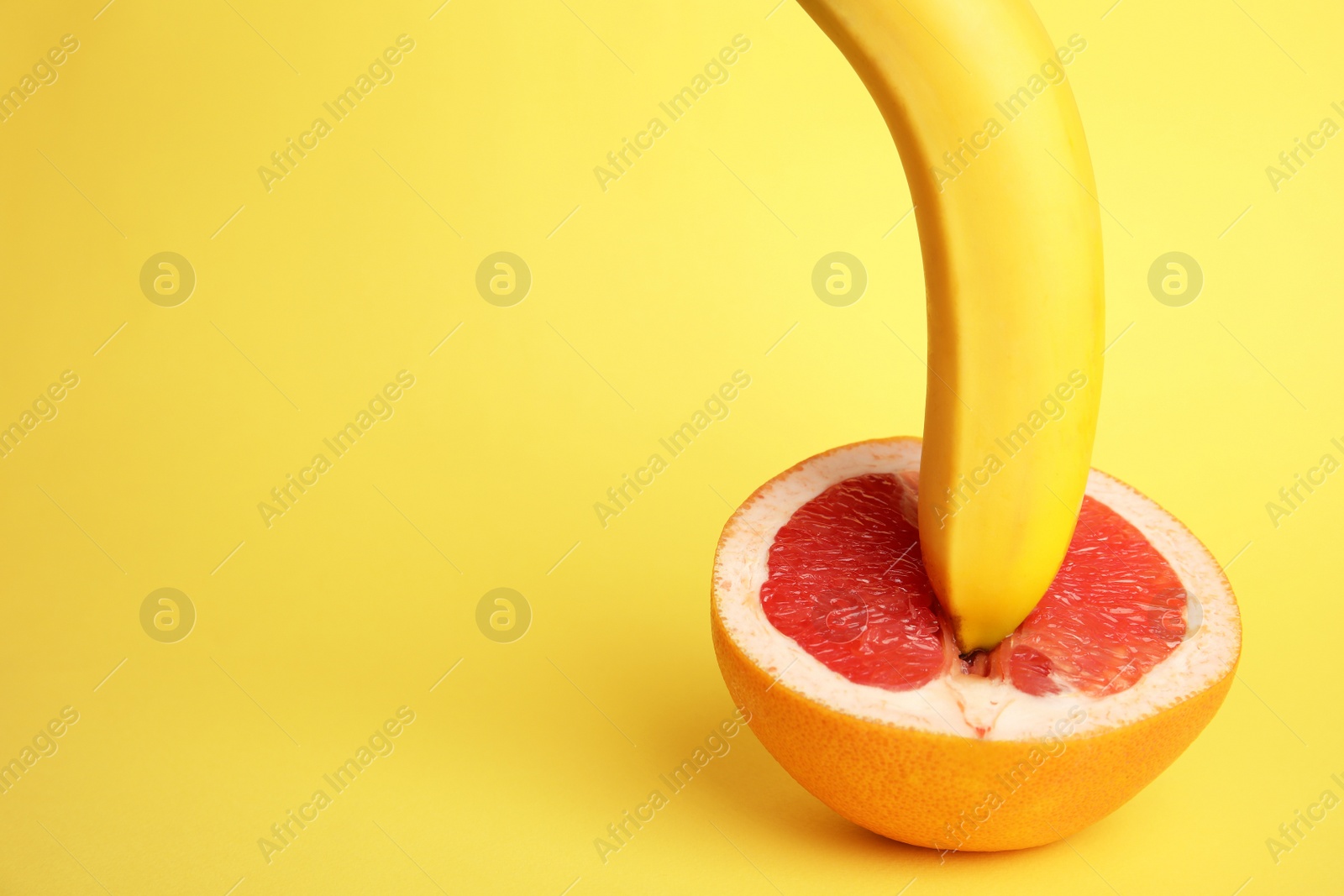 Photo of Fresh grapefruit and banana on yellow background, space for text. Sex concept