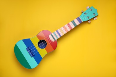 Photo of Colorful ukulele on yellow background, top view. String musical instrument
