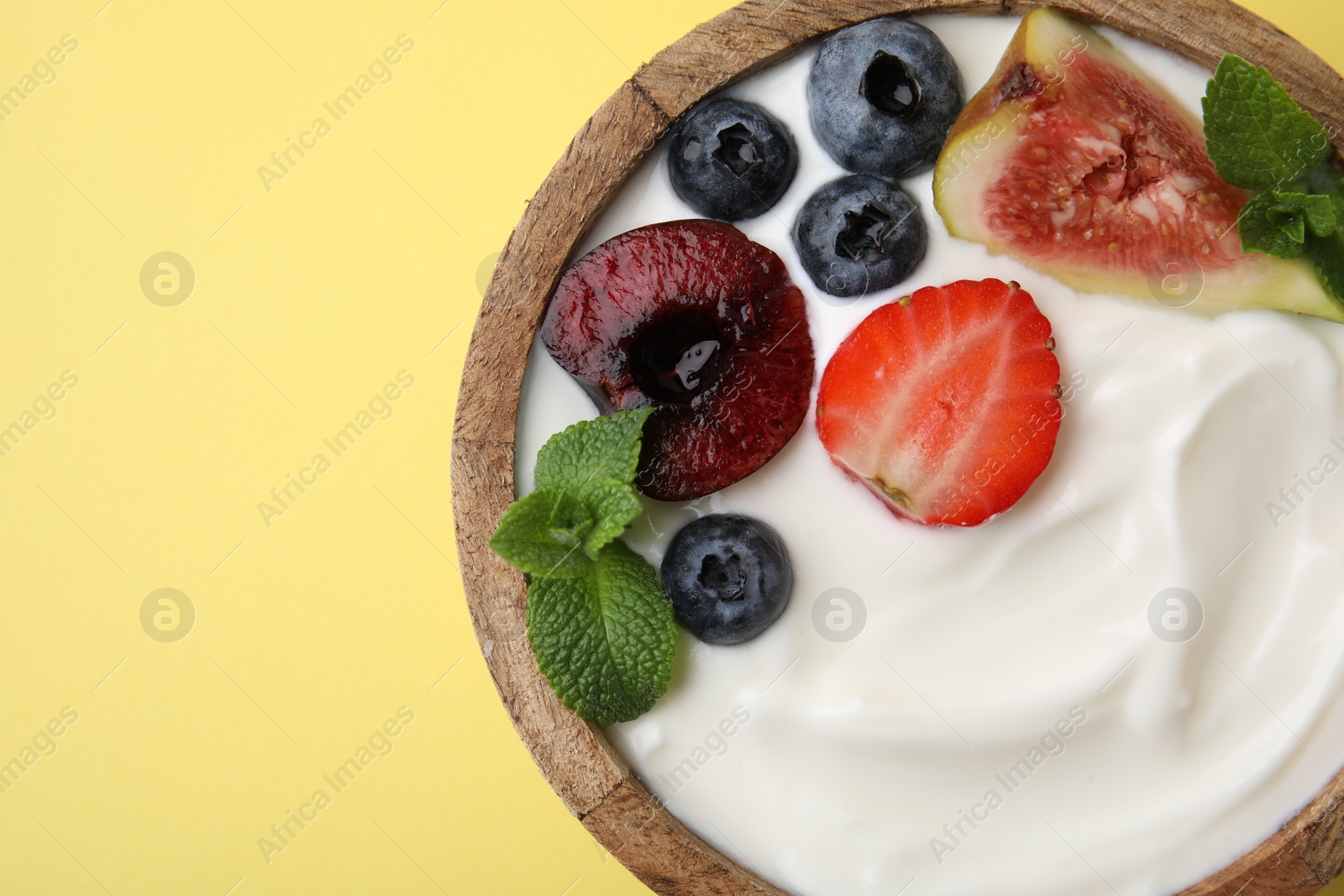 Photo of Bowl with yogurt, berries, fruits and mint on yellow background, top view. Space for text