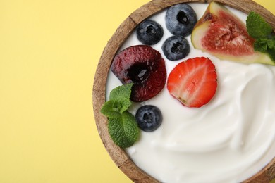 Bowl with yogurt, berries, fruits and mint on yellow background, top view. Space for text