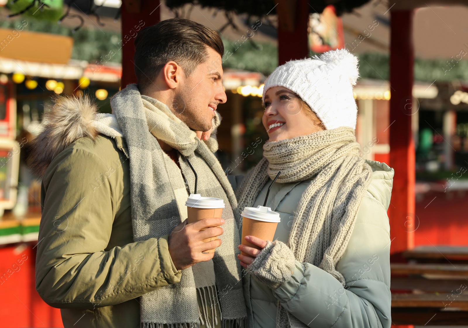 Photo of Happy couple in warm clothes with drinks at winter fair. Christmas season