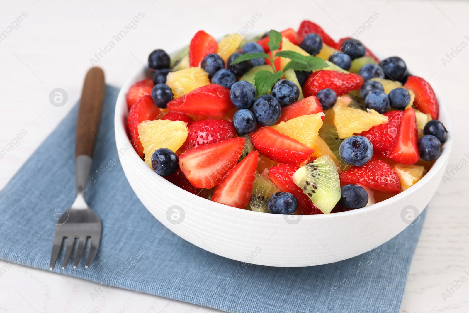 Photo of Delicious fresh fruit salad in bowl served on white table, closeup