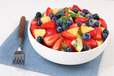 Delicious fresh fruit salad in bowl served on white table, closeup