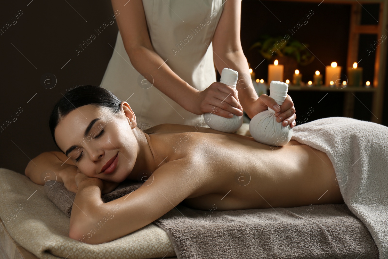 Photo of Young woman receiving herbal bag massage in spa salon