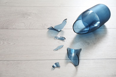 Photo of Broken blue glass vase on wooden floor. Space for text