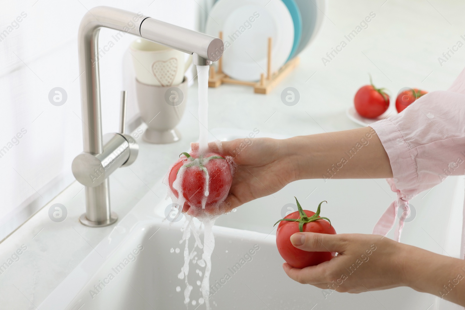 Photo of Woman washing fresh ripe tomatoes under tap water in kitchen, closeup