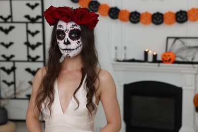 Photo of Young woman in scary bride costume with sugar skull makeup and flower crown indoors, space for text. Halloween celebration