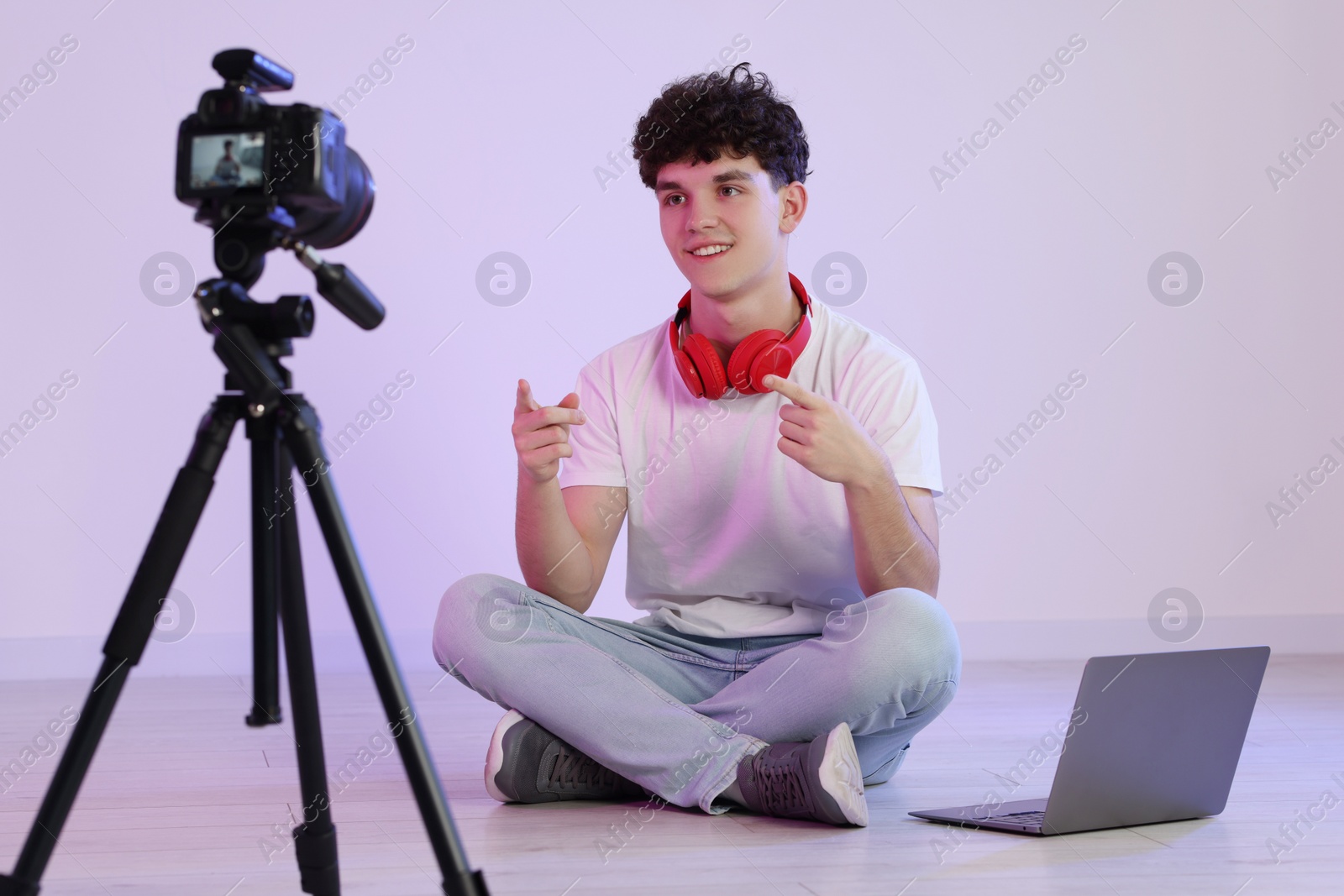 Photo of Smiling teenage blogger with laptop explaining something while streaming indoors