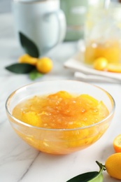 Photo of Delicious kumquat jam in glass bowl on white marble table