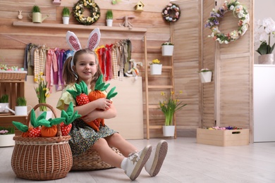 Photo of Adorable little girl with bunny ears and toy carrots in Easter photo zone