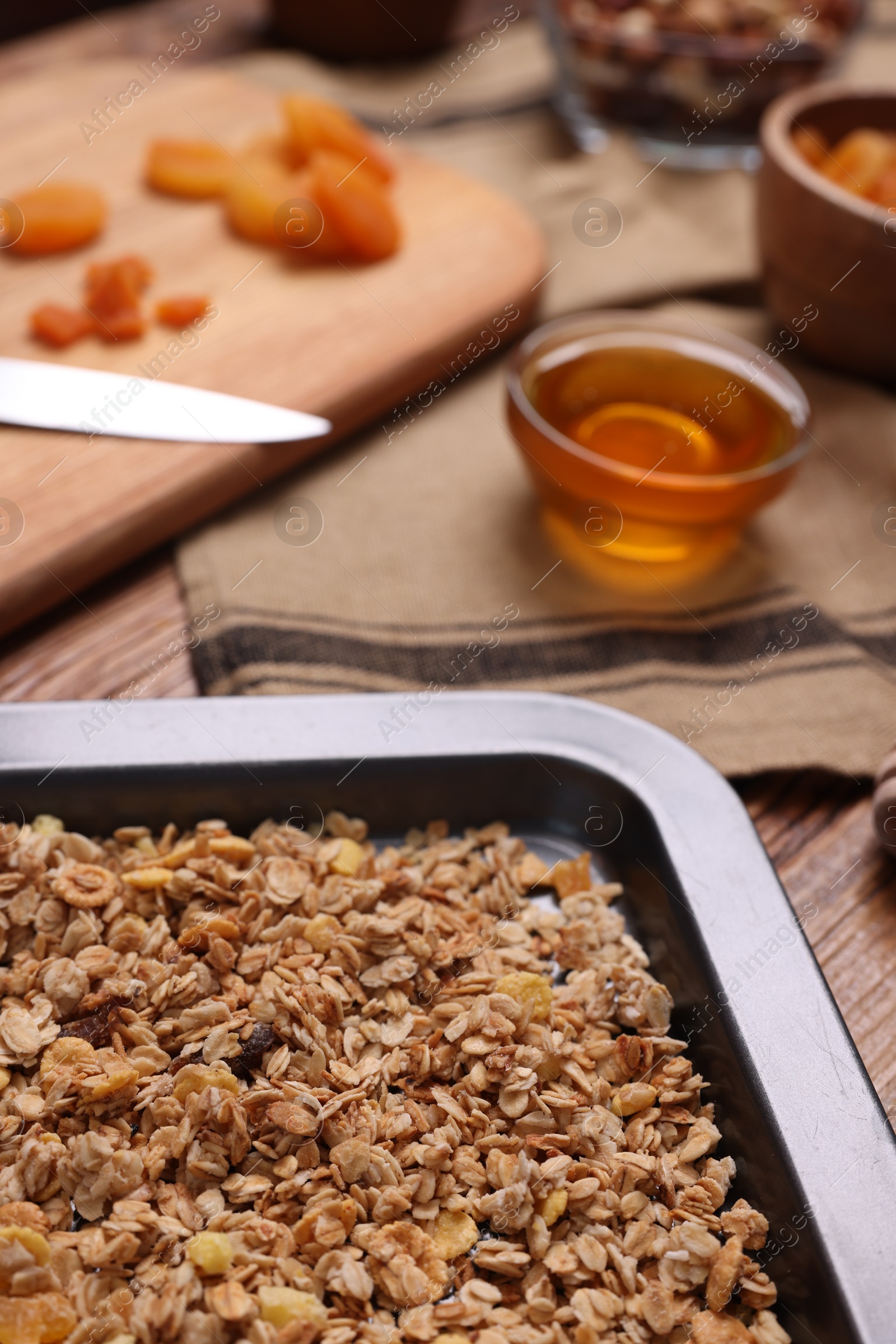 Photo of Making granola. Baking tray with mixture of oat flakes and other ingredients on wooden table, closeup