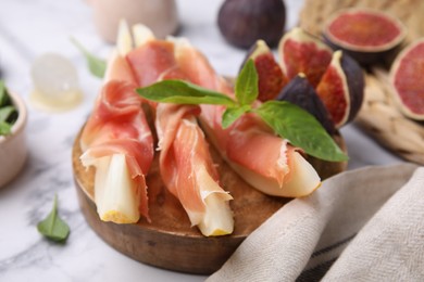 Photo of Tasty melon, jamon and figs served on white marble table, closeup