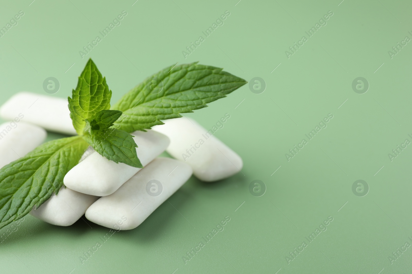 Photo of Tasty white chewing gums and mint leaves on light green background, closeup. Space for text