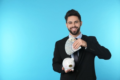 Portrait of happy young businessman with money and piggy bank on color background. Space for text
