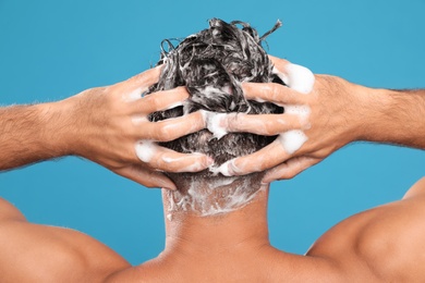 Photo of Man washing hair on light blue background, back view