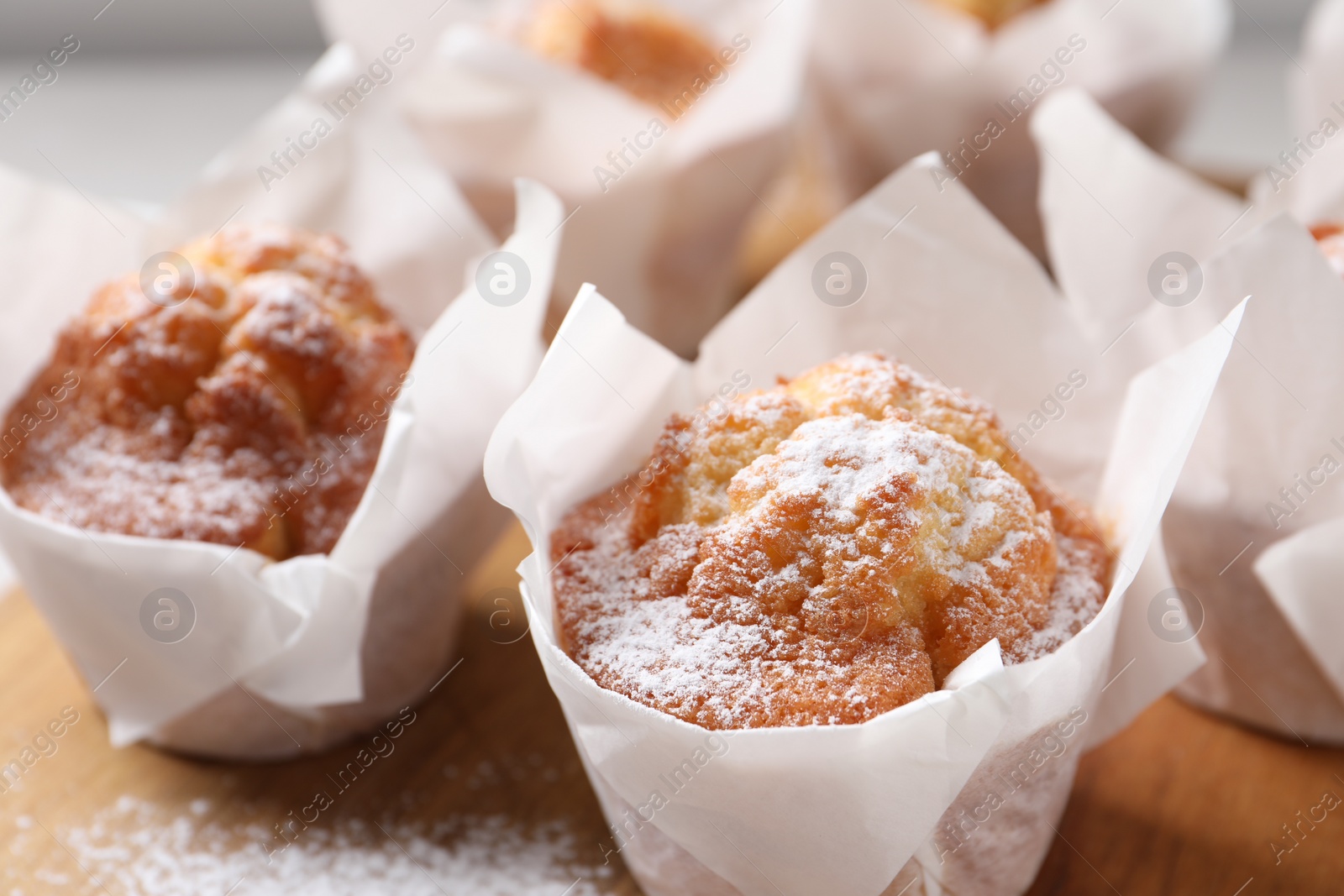 Photo of Delicious muffins with powdered sugar on wooden board, closeup