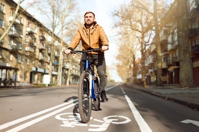 Happy handsome man riding bicycle on lane in city, low angle view