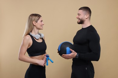 Photo of Athletic people with skipping rope, headphones and medicine ball on light brown background