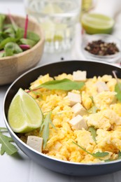 Frying pan with delicious scrambled eggs, tofu and lime on white table, closeup