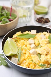 Photo of Frying pan with delicious scrambled eggs, tofu and lime on white table, closeup