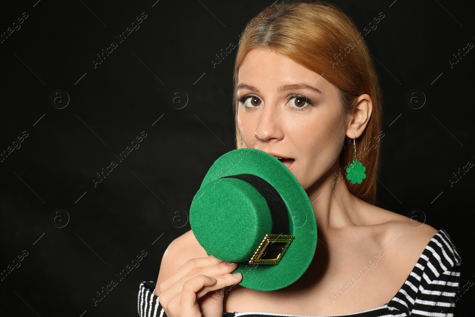 Photo of Young woman with green leprechaun hat on black background, space for text. St. Patrick's Day celebration