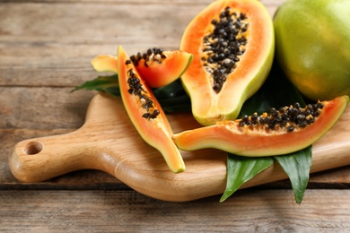 Photo of Fresh ripe papaya fruits with green leaves on wooden table