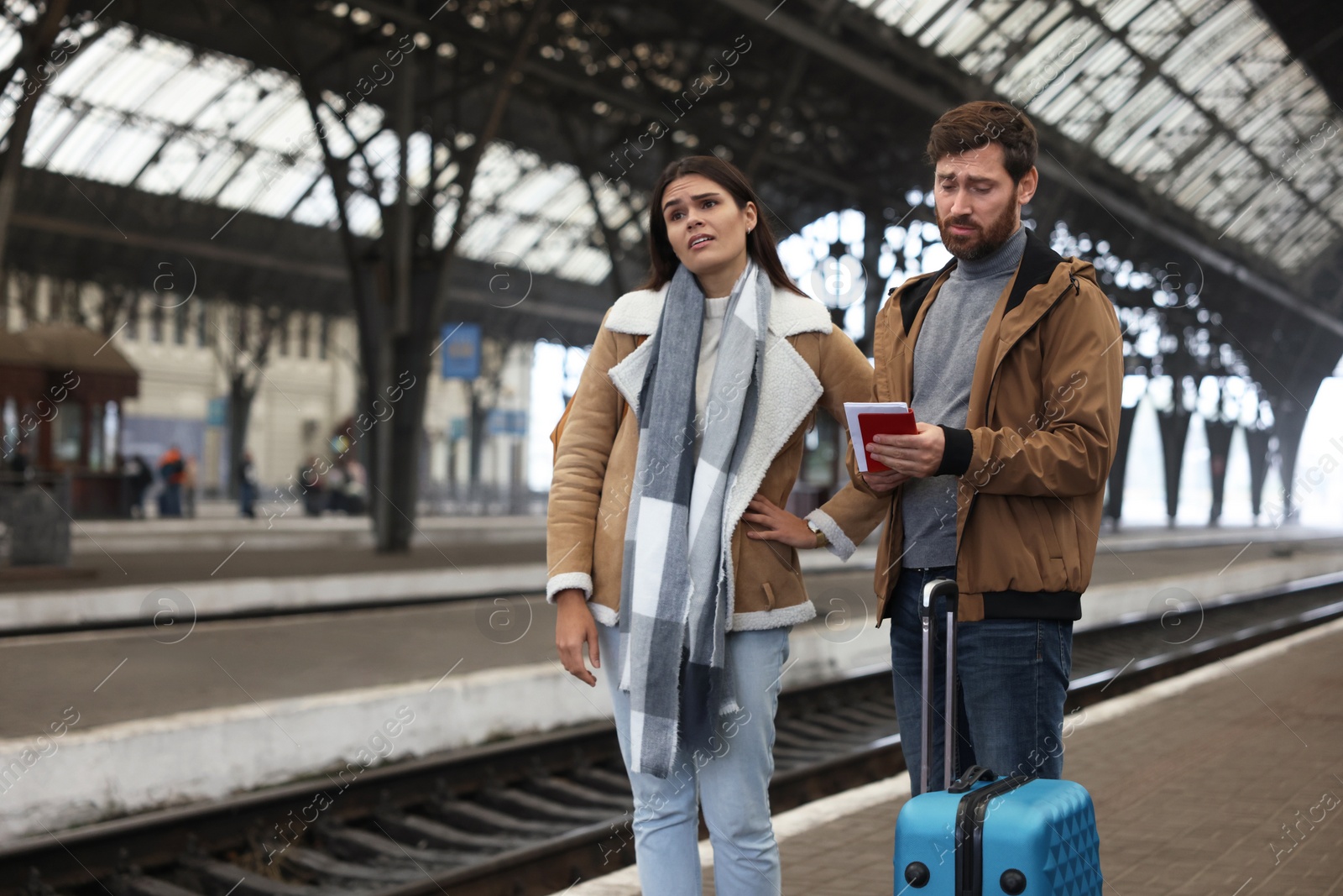 Photo of Being late. Worried couple with suitcase waiting at train station, space for text