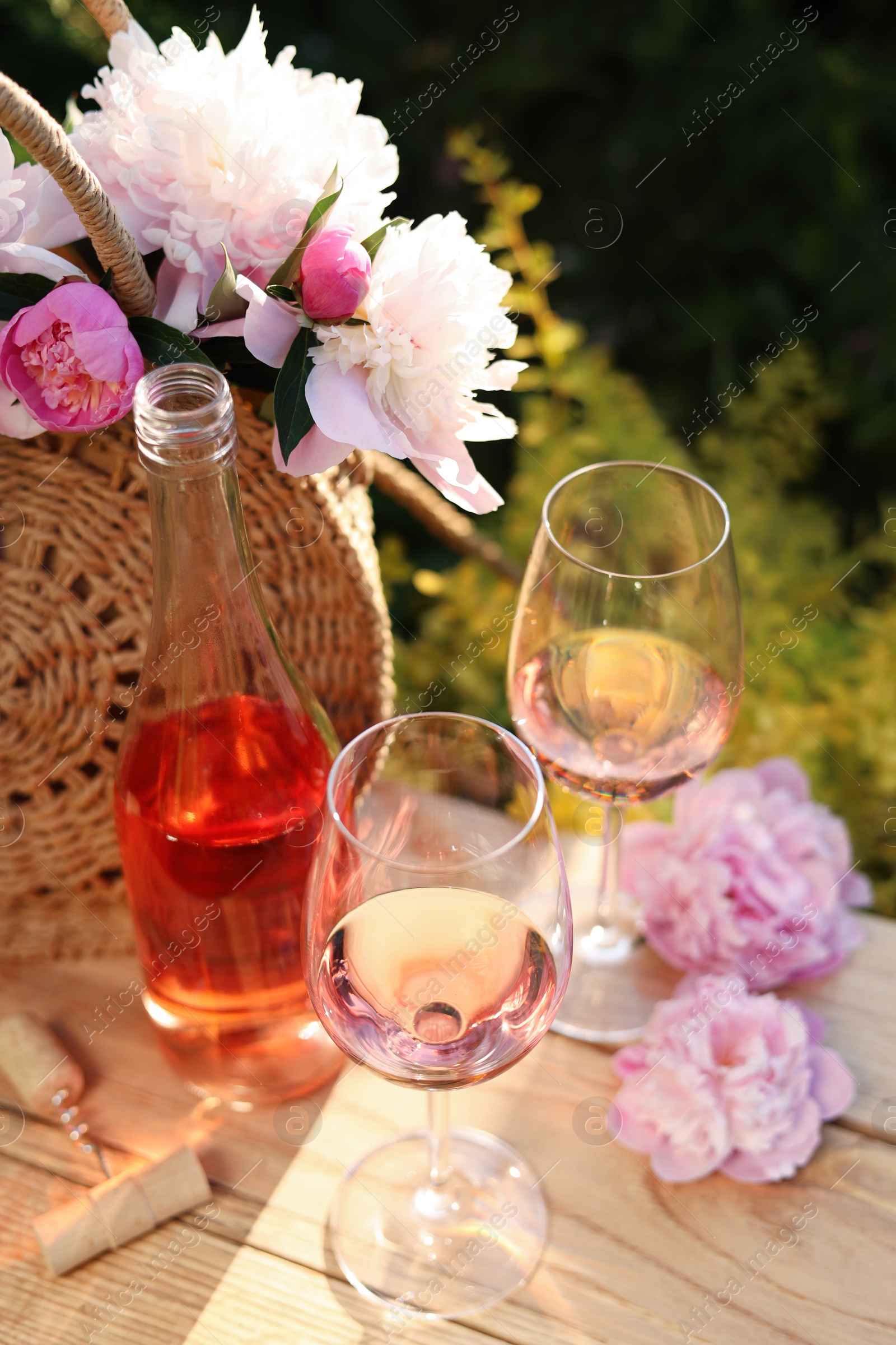 Photo of Bottle and glasses of rose wine near beautiful peonies on wooden table in garden