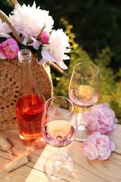 Photo of Bottle and glassesrose wine near beautiful peonies on wooden table in garden
