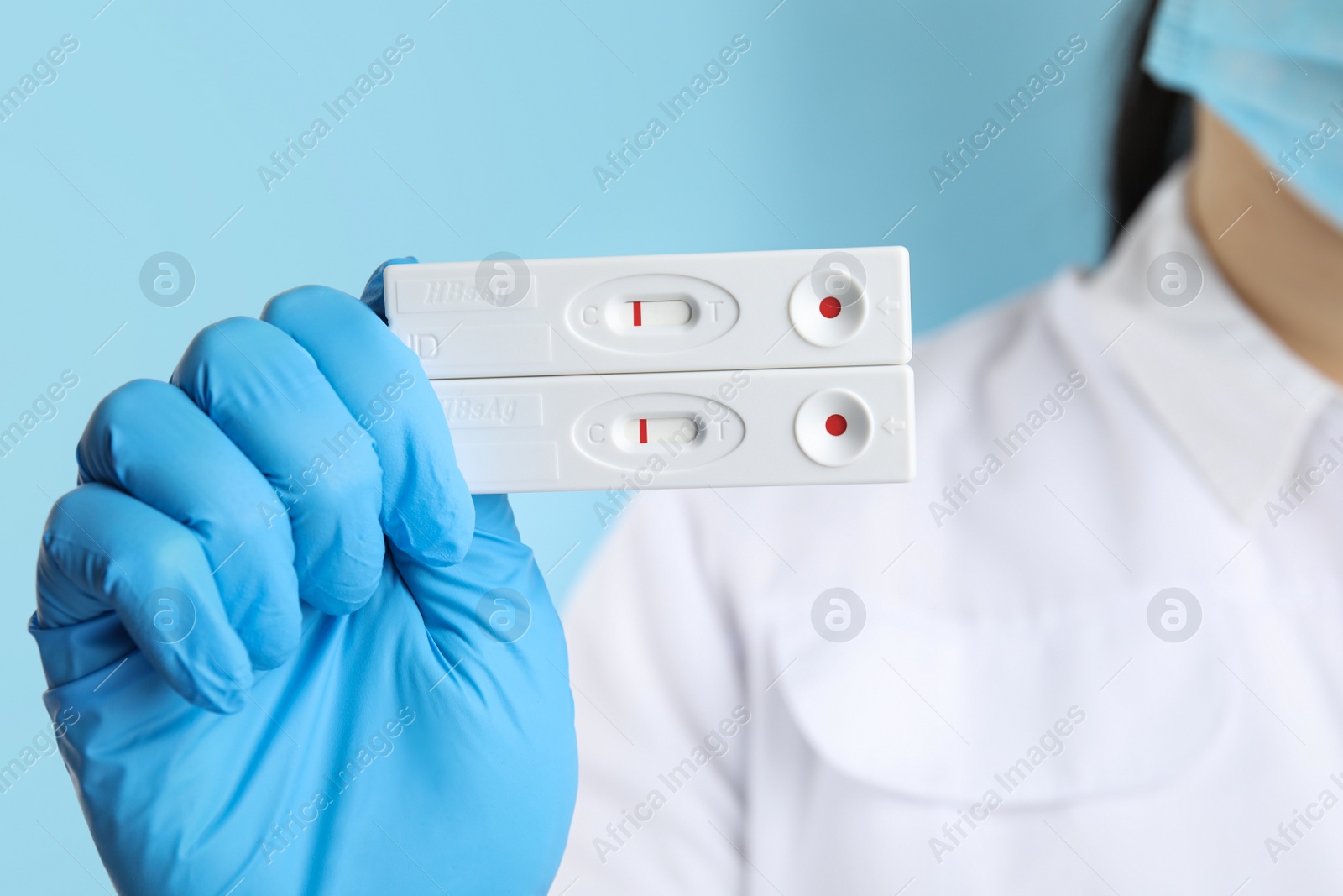 Photo of Doctor holding two disposable express tests for hepatitis on light blue background, closeup