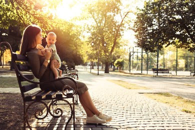 Young mother with her cute baby on bench in park