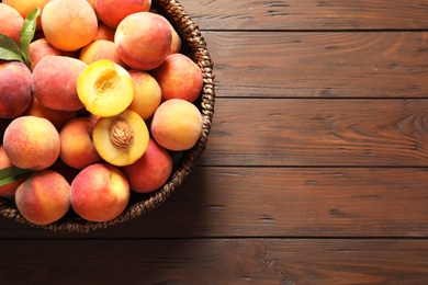 Wicker basket with fresh sweet peaches on wooden table, top view