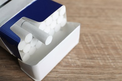 Photo of Cigarettes in pack on wooden table, closeup. Space for text