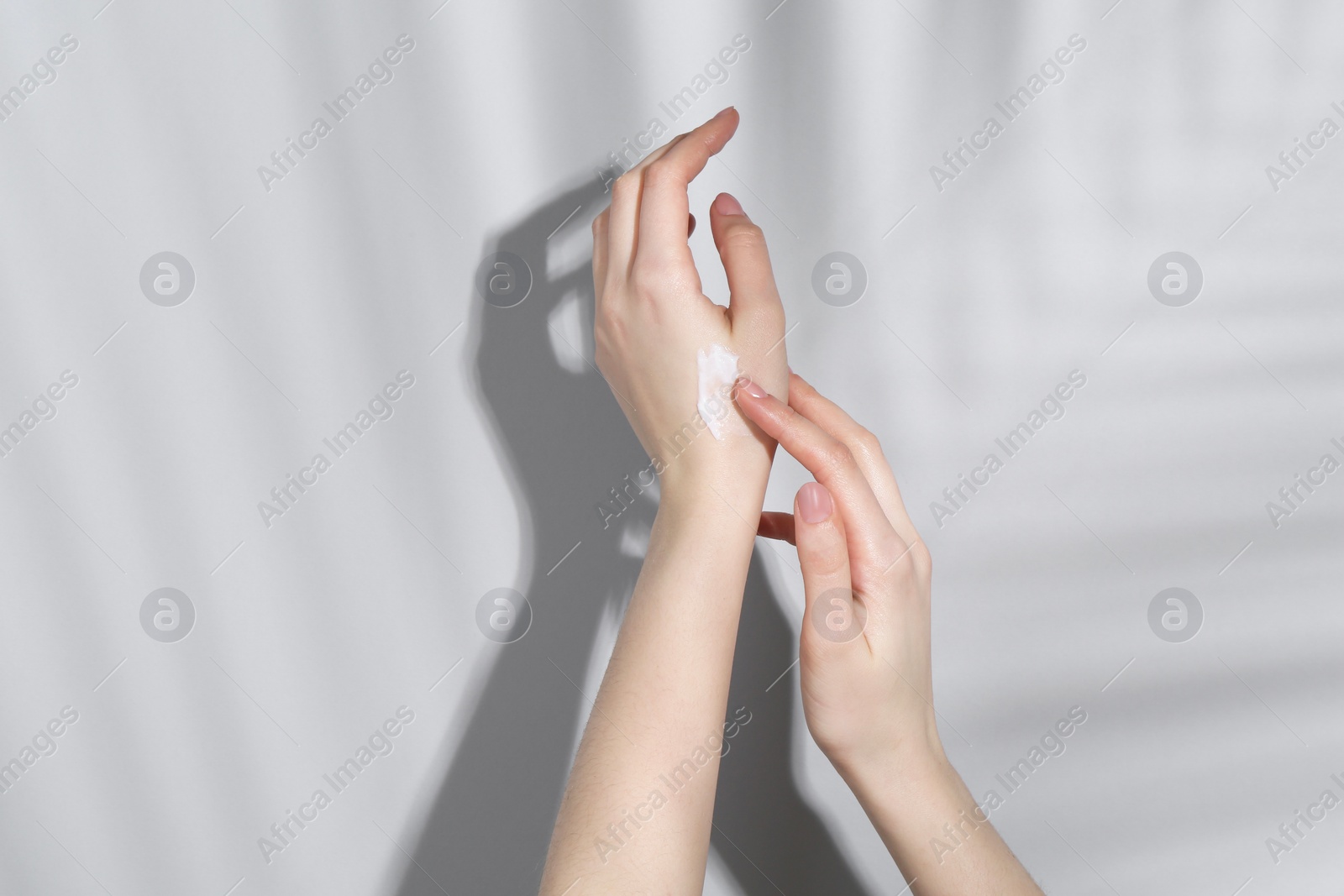 Photo of Woman applying cream on her hand against grey background, closeup