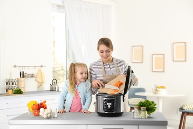 Mother and daughter preparing food with modern multi cooker in kitchen