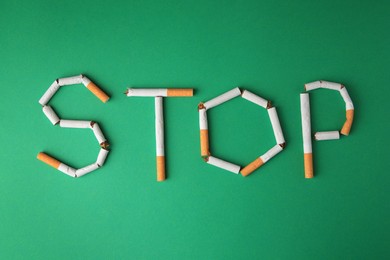 Photo of Word Stop made of broken cigarettes on green background, flat lay. Stop smoking concept