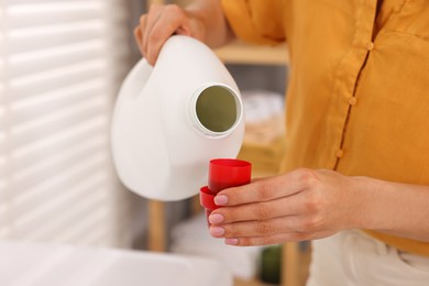Photo of Woman pouring laundry detergent into cap indoors, closeup