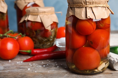 Photo of Pickled tomatoes in glass jars and products on wooden table, closeup view