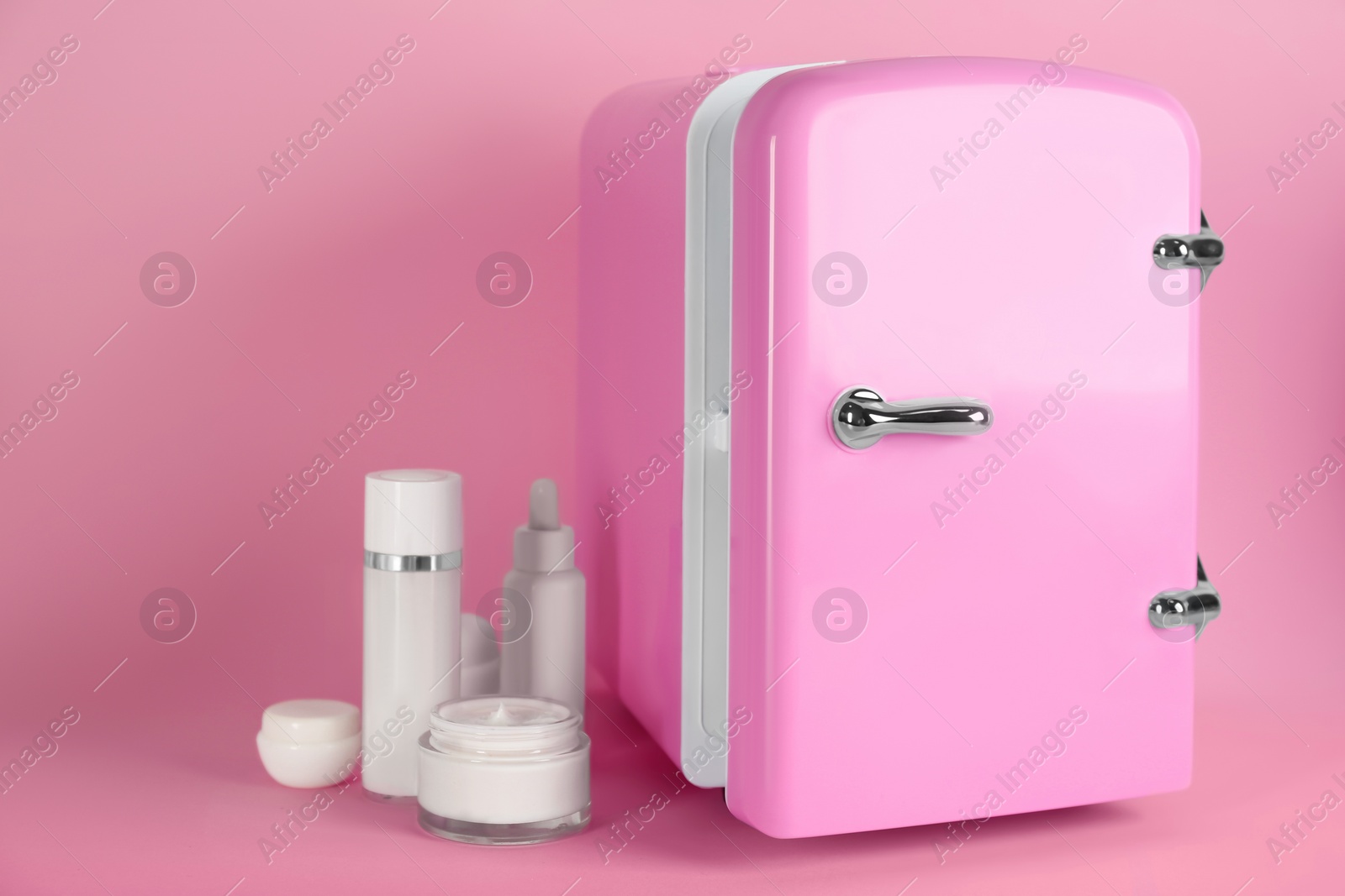 Photo of Cosmetic refrigerator and skin care products on pink background