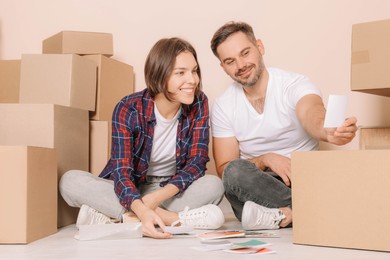 Happy couple surrounded by moving boxes choosing colors in new apartment