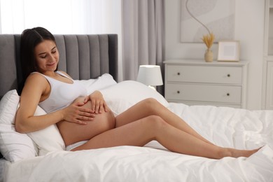 Photo of Beautiful pregnant woman in stylish comfortable underwear making heart with hands on her belly in bedroom